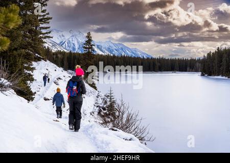 Eine Gruppe von Menschen, die auf einem Winterwanderweg entlang des Johnson Lake im Banff National Park Canada wandern Stockfoto