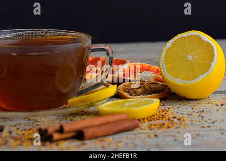 Glas Tasse Tee mit Zimtstangen auf Holztisch Hintergrund. Zimtschnecken, Sternanise, Zitrone und Trockenfrüchte. Schwarzer Hintergrund. Makrobild Stockfoto