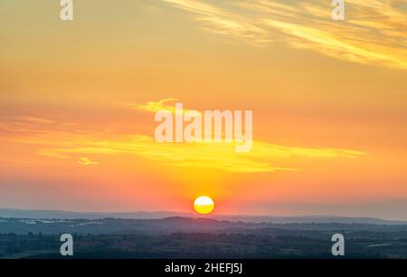 Blick vom Gipfel des Worcestershire Beacon. Die Sonne geht über den klaren Horizont auf, über die mit Bäumen und Feldern bedeckte Landschaft, an einem Mittsommermorgen, auf den berühmten Berg Stockfoto