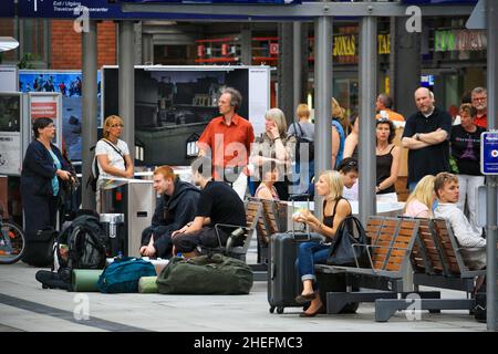 Im Sommer sitzen und stehen Menschen aus Europa auf dem Bahnsteig des Hamburger Hauptbahnhofs oder des Hauptbahnhofs, die auf die Abfahrt warten. Stockfoto