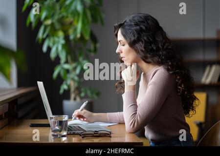 Junge Akademikerin, die sich den Laptop-Bildschirm ansieht, recherchiert online, während sie in der Bibliothek arbeitet Stockfoto