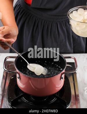 Indonesische weibliche Hand Put Sugar Palm Fruit (Kolang Kaling oder Cangkaleng) auf ein kochendes Wasser in einer Pfanne in der Indonesischen Küche. Prozess, Der Manisan Kol Stockfoto