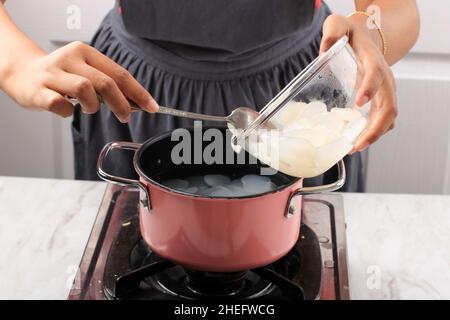 Femalen Asian Hand Gießen Sie Zuckerpalmenfrucht (Kolang Kaling oder Cangkaleng) auf ein kochendes Wasser in einer Pfanne in der Indonesischen Küche. Prozess, Der Manisan Kolang Macht Stockfoto