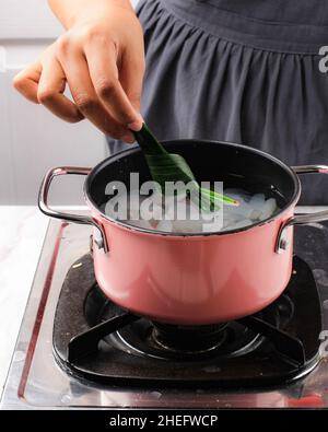 Legen Sie Pandan Blatt auf eine rosa Pfanne enthalten Zucker Palme Frucht (Kolang Kaling). Kochvorgang Herstellung von Manisan Cangkaleng für Ramadhan Frühstück Takjil Stockfoto