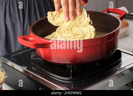 Von Hand Nudeln in kochendes Wasser auf der Pfanne geben. Instant-Nudeln kochen (Mie telur). Kochvorgang in der Küche Stockfoto