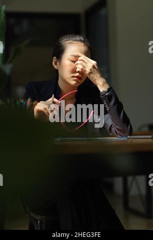 Porträt einer müden jungen Geschäftsfrau mit Brille, die an ihrem Schreibtisch sitzt. Erschöpfte, überarbeiteter Unternehmer. Stockfoto