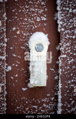 Verschneite Türklingel auf einer braunen Holzoberfläche. Stockfoto