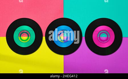 Drei Vinyl-CDs im flachen Lay-Format auf einem bunten, lebendigen Retro-Hintergrund. Stockfoto