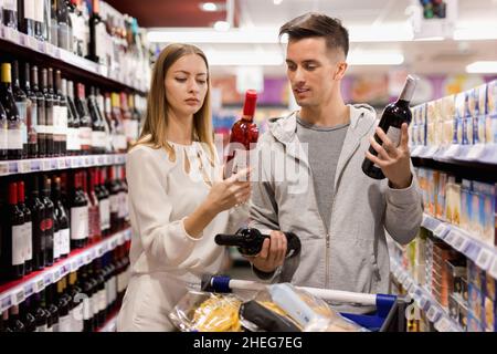 Porträt eines jungen Mannes und einer jungen Frau, die im Lebensmittelgeschäft eine Flasche Wein auswählen Stockfoto