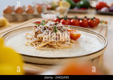 Teller mit Haufen italienischer Pasta mit gebratenem Hackfleisch, bestreut mit geriebenem Käse, zwischen frischem Gemüse und Eiern stehend Stockfoto
