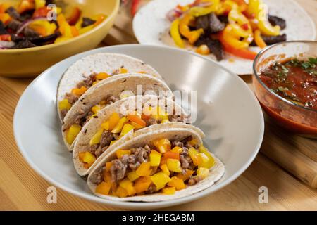 Weißer Porzellanteller mit traditionellem mexikanischen Taco, umgeben von hausgemachter Tomatensauce und Gemüseeintopf Stockfoto