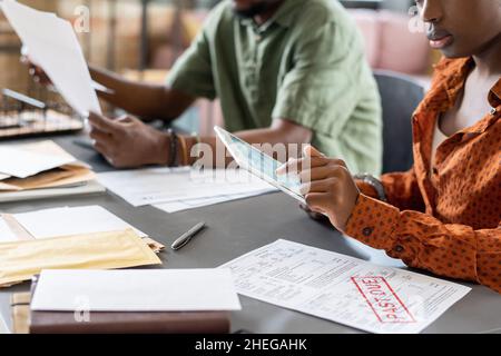 Junge afrikanische Auditorin zeigt auf Tablet-Bildschirm, während sie Online-Finanzdaten überprüft und mit Papieren arbeitet Stockfoto