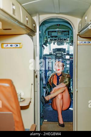 Auf einem Board von Verkehrsflugzeugen. Stewardess in blauer Uniform. Stewardess in Uniform in der Passagierkabine des Flugzeugs. Junge Frau in Stockfoto