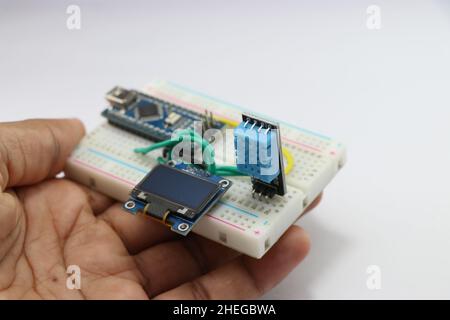 Feuchtigkeits- und Temperaturmessmodul für Arduino-Projekte mit OLED-Schaltung auf einem in der Hand gehaltenen Breadboard, das das Konzept der kreativen Idee zeigt Stockfoto