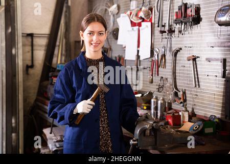Porträt einer jungen lächelnden Frau in Uniform, die mit einem Hammer in der Hand Stockfoto