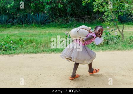 Omo River, Äthiopien - 30. November 2020: Süßes und junges afrikanisches Mädchen mit schwerer Tasche auf der Landstraße Stockfoto