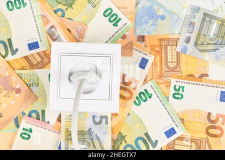 Weiße Steckdose mit Stecker auf Euro-Banknoten Hintergrund. Steigende Stromkosten, teures Energiekonzept Stockfoto