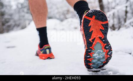 Unbekannter Mann, der am Wintertag im Schnee läuft, Nahaufnahme von Schuh-Sneakern Stockfoto