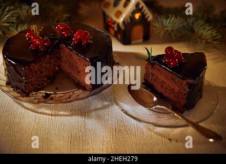 Der Mozartkuchen besteht aus 3 Schichten Schokoladenkuchen, der mit Cognac mit frischen Beeren und Rosmarin auf einem transparenten Teller getränkt ist Stockfoto