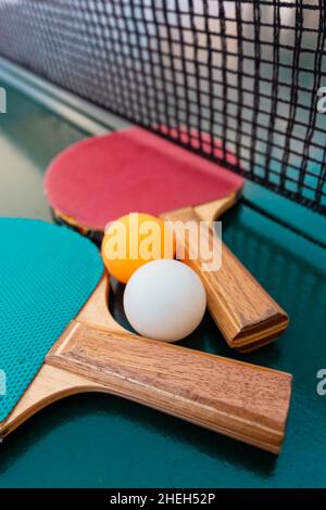 Tischtennisschläger und Tischtennisbälle auf grüner Tischfläche mit Netz, selektiver Fokussierung Stockfoto