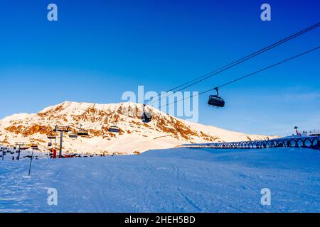 Alpe d'Huez, Frankreich - 30.12.2021 : Skiliftseilbahn am Abend auf alpinem Bergwintergebiet. Ski Sessellift Seilbahn mit Menschen. Typisch fren Stockfoto