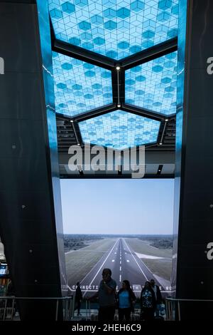 Passagiere, die vor einem großen digitalen Werbebildschirm in der Abflughalle am Flughafen Manchester, England, vorbeikommen Stockfoto