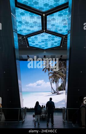 Passagiere, die vor einem großen digitalen Werbebildschirm in der Abflughalle am Flughafen Manchester, England, vorbeikommen Stockfoto