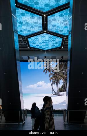 Passagiere, die vor einem großen digitalen Werbebildschirm in der Abflughalle am Flughafen Manchester, England, vorbeikommen Stockfoto