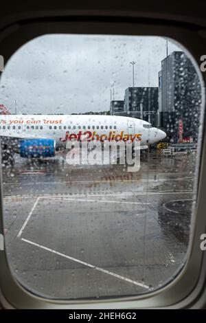 Jet 2 Ferienflugzeug durch das Fenster eines Flugzeugs im Regen auf dem Boden am Flughafen Manchester, England, Großbritannien, gesehen Stockfoto