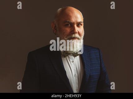 Porträt eines lächelnden und selbstbewussten reifen balding Senior Geschäftsmann, trägt einen Anzug und eine Krawatte, vor einer grauen Wand mit Copy-Space. Stockfoto