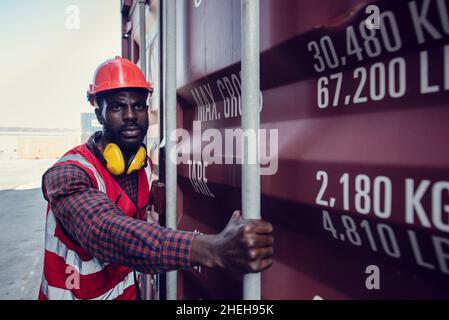 Afroamerikanische Arbeiter öffnen Container für Inspektionen und überprüfen, ob Reparaturen in Containern durchgeführt wurden. Stockfoto