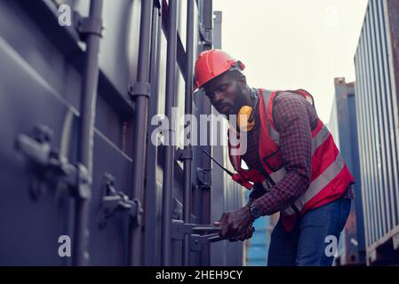 Afroamerikanische Arbeiter öffnen Container für Inspektionen und überprüfen, ob Reparaturen in Containern durchgeführt wurden. Stockfoto