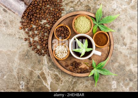 Kaffeebohnen, eine Tasse frisch gebrühten Kaffee mit Cannabis, Morijuana-Samen und Blättern auf einem Tablett. Draufsicht Stockfoto