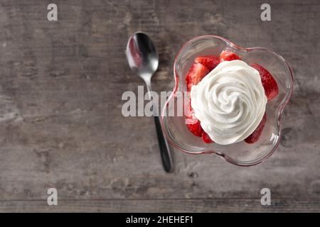 Erdbeeren und Schlagsahne in Eisglas auf einem Holztisch Stockfoto
