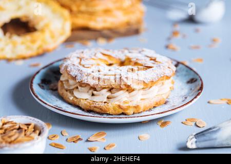 Traditionelles französisches Dessert namens Paris Brest auf grauem Hintergrund mit Puderzucker und Mandelblättern und Mandelcreme dazwischen Stockfoto