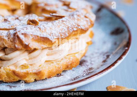 Traditionelles französisches Dessert namens Paris Brest auf grauem Hintergrund mit Puderzucker und Mandelblättern und Mandelcreme dazwischen Stockfoto
