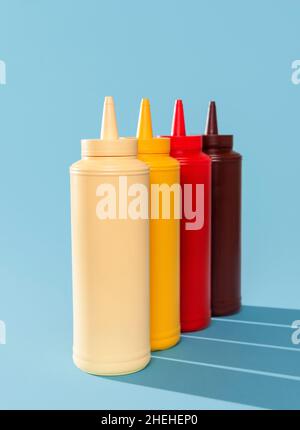 Nahaufnahme mit mehreren Saucenflaschen auf einem blauen Tisch. Verschiedene Soßen in Plastikflaschen isoliert auf blauem Hintergrund. Stockfoto