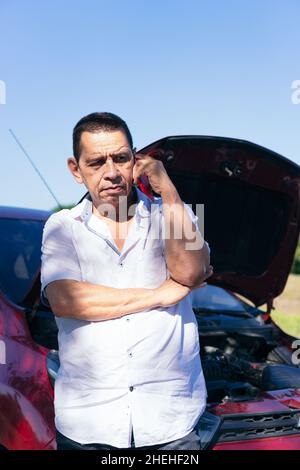 Reifer Mann, der neben einem kaputten Auto auf dem Handy spricht Stockfoto