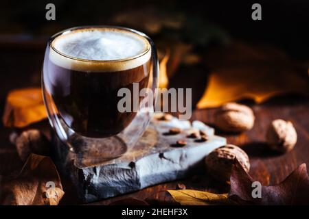 Tasse Kaffee in doppelter Glastasse in herbstlicher Stimmung mit Blättern und Kaffeebohnen Details in Einstellung und Hintergrund Stockfoto