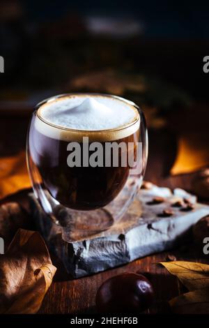Tasse Kaffee in doppelter Glastasse in herbstlicher Stimmung mit Blättern und Kaffeebohnen Details in Einstellung und Hintergrund Stockfoto