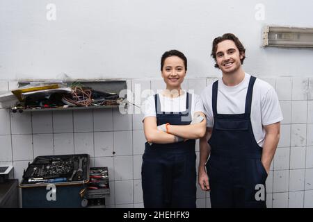 Lächelnde Mechaniker, die die Kamera in der Nähe von Werkzeugen im Autodienst betrachten Stockfoto