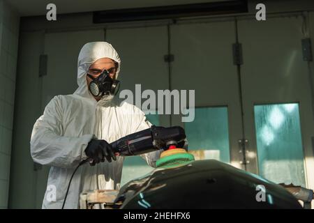 Arbeiter in Hazmat Anzug und Atemschutzmaske Polieren Auto-Teil in Betrieb Stockfoto