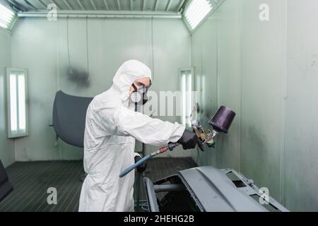 Arbeiter in Atemschutzmaske und Gefahrgut Anzug Färbung Auto Teil während der Arbeit im Service Stockfoto
