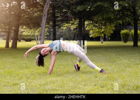 Junge Frau praktiziert Yoga im öffentlichen Park bei Sonnenaufgang Stockfoto