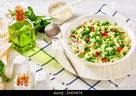 Risi e Bisi, venezianische dicke arborio-Reissuppe mit Frühlingserbsen und Schinkenstückchen in einer weißen Schüssel auf einem Holztisch mit Zutaten, italienische Küche, Stockfoto