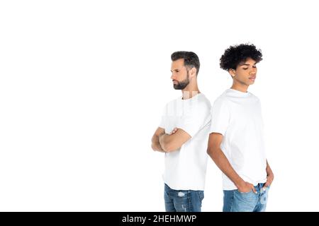 Beleidigte interrassische Männer, die mit gekreuzten Armen und Händen in weißen, isolierten Taschen Rücken an Rücken stehen Stockfoto