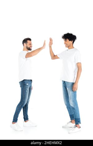 In voller Länge Ansicht von interracial Freunde in Jeans und T-Shirts geben High Five auf weiß Stockfoto