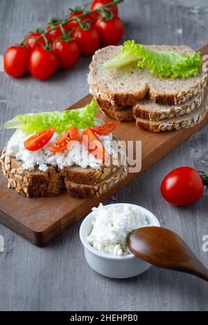 Roggenbrotscheiben mit Quark und Tomaten auf Holzplatte Stockfoto