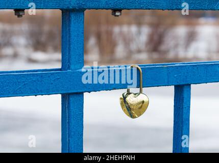 Irkutsk, Russland- 30. März 2021: Geschlossene, goldene Herzschlösser oder Liebesschlösser auf blauer Brücke auf verschwommenem Winterhintergrund. Hochzeit oder romantische Koncep Stockfoto