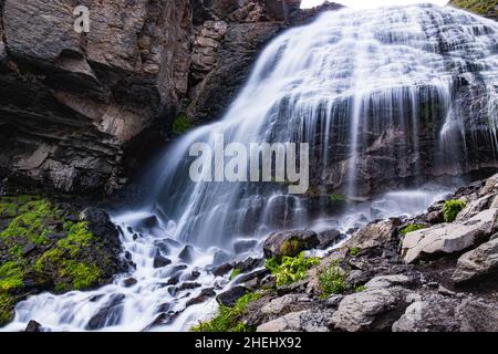 Ein fantastischer Gebirgswasserfall, die stürmischen Ströme eines Gebirgsflusses fallen an einem sonnigen Tag aus einer großen Höhe auf die Felsen Stockfoto